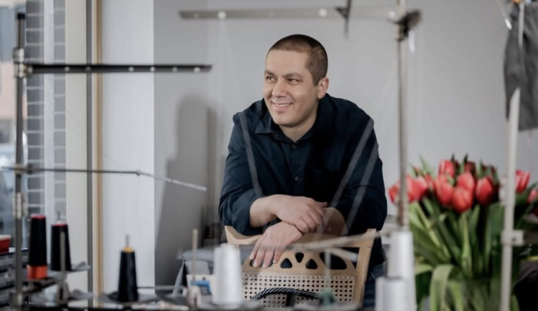 Veli Sahin achter de balie van Karin's Kledingreparatie met meetlint om zijn nek